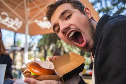 Happy guy looking at the camera, his mouth is wide open. He is holding burger Stock Photos