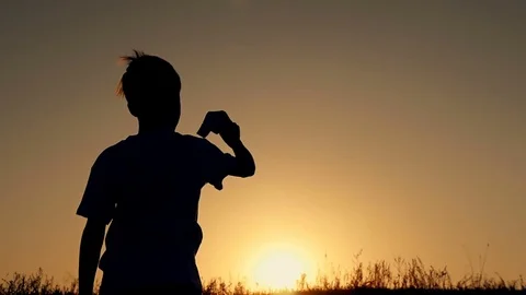 Happy guy playing with a paper airplane in a field in the sun. Silhouette at Stock Footage