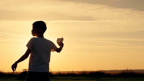 Happy guy playing with a paper airplane in a field in the sun. Silhouette at Stock Footage 80984878