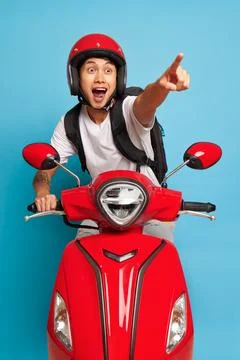 Happy guy in red helmet posing on red scooter, one hand on handle bar, another Photos