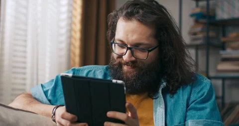 A happy guy relaxes on the couch with a tablet in hand, browses social media 库存影片 218201766