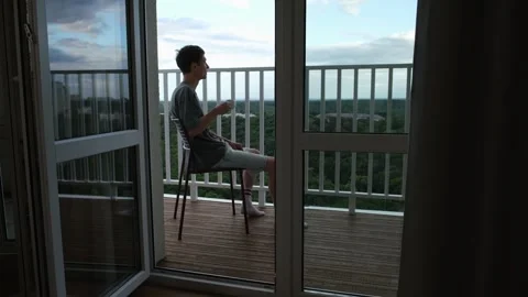 Happy guy sitting on the terrace drinks coffee. Realistic scene of enjoying the Stock Footage 312327400