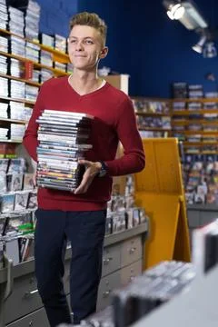 Happy guy standing with stack of DVDs in hands in shop Stock Photos