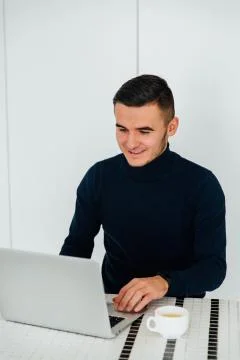 Happy guy using a laptop while sitting for the table with cup of tea Stock Photos