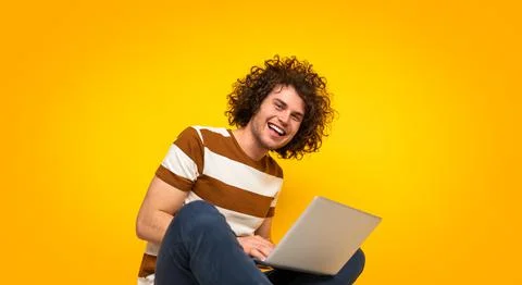 Happy guy using netbook and smiling at camera in yellow studio Stock Photos