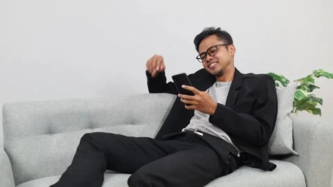 Happy Handsome Asian Man Using Smartphone in Cozy Living Room at Home Vídeos de archivo 336509986