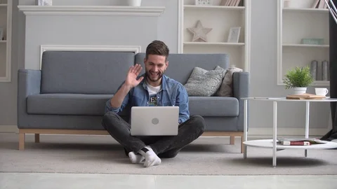Happy handsome bearded man videocalling on laptop while sitting on floor at home Stock Footage 129166720