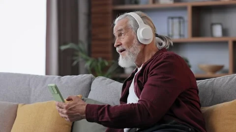 Happy handsome elderly gray-haired man in white headphones enjoy listening Stock Footage 197413021