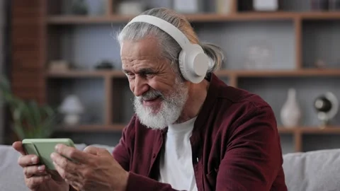 Happy handsome elderly gray-haired man in white headphones holding smartphone Stock Footage 197413045
