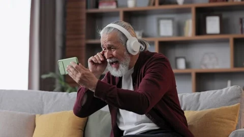 Happy handsome elderly gray-haired man in white headphones holding smartphone Stock Footage 219644946