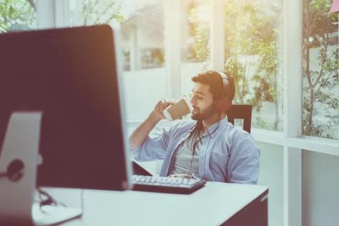 Happy handsome man with beard drinking coffee and listening to music online a Stock Photos