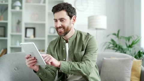 Happy handsome man using digital tablet sitting on sofa in living room at home.  Stock Footage 291190071