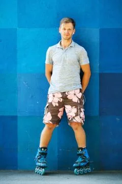 Happy handsome young roller in inline skates sitting against blue wall. Foto stock