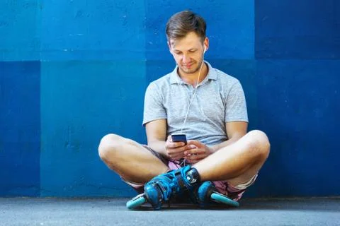 Happy handsome young roller in inline skates sitting against blue wall. Foto stock