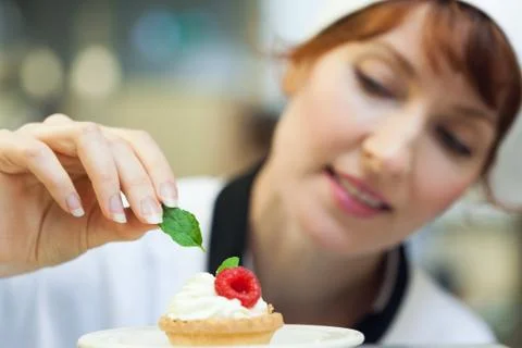 Happy head chef putting mint leaf on little cake Stock Photos