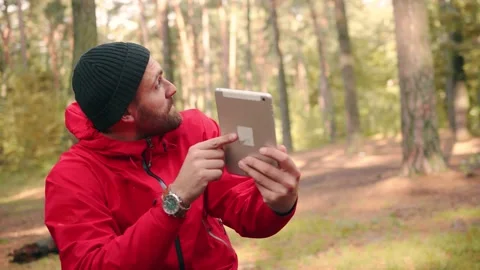 Happy hiker man in hat sitting in park at day time and talking over video call Stock Footage 147069876