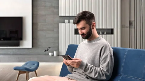 Happy Hispanic man chatting use smartphone online communication sitting on couch Stock Footage 229715000