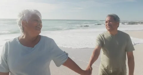 Happy hispanic senior couple walking on beach at sunset Stock Footage 345712359