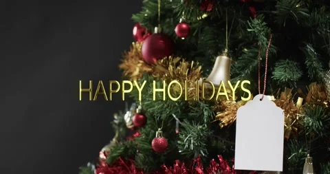 Happy holidays text in gold over decorated christmas tree and blank gift tag Stock Footage 329018067