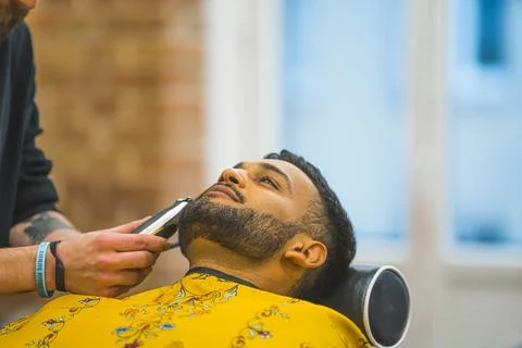 Happy indian client having his beard trimmed by a profssional barber in the Stock Photos