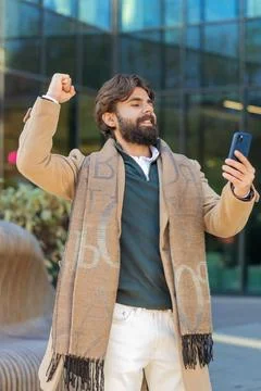 Happy Indian man using smartphone celebrating victory win good message news on Stock Photos