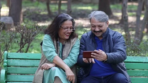 Happy Indian senior couple using smart phone at park, watching video. Stock Footage 258013359