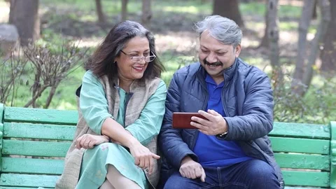Happy Indian senior couple using smart phone at park, watching video. Stock Footage 258013374