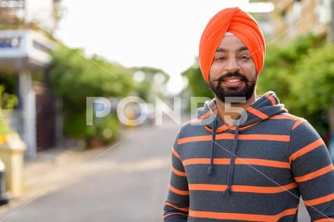 Happy Indian Sikh man smiling outdoors and wearing orange turban Stock Photos