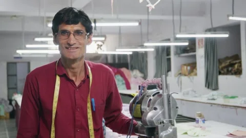 Happy Indian tailor man facing the camera in a garment workshop Stock Footage 243633227