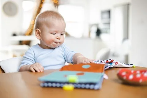 Happy infant sitting at dining table and playing with his toy in traditional Stock Photos