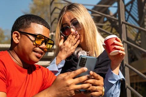 Happy interracial couple checking cell phone outdoors. Stock Photos