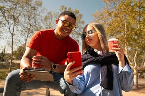 Happy interracial couple checking cell phone outdoors. Stock Photos