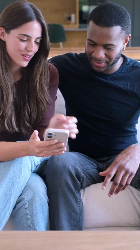Happy interracial couple relaxing on a sofa at home, laughing and having fun 動画素材 346608100