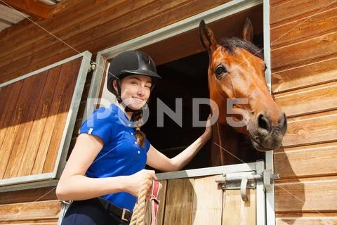 Happy jockey girl stroking horse at riding stable Stock Photos