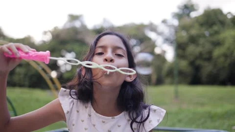 Happy kid blowing soap bubbles with public park on background Video stock 303611084
