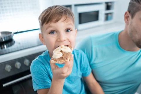 Happy kid boy and father eating healthy peanut butter toast at home kitchen Stock Photos