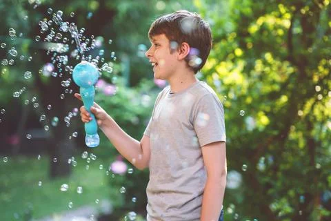 Happy kid boy having fun with blowing soap bubble blower. Preteen child playing Stock Photos