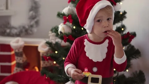 Happy kid boy in Santa hat and Christmas clothes opens candy and eats. Stock Footage 140636751