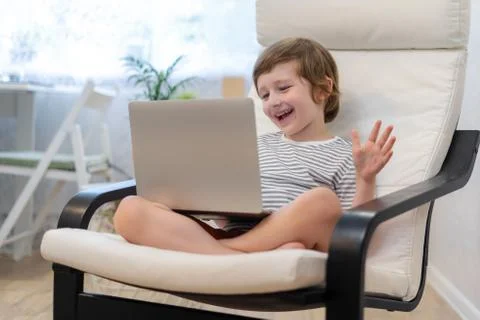 Happy kid boy sit on computer using laptop and having a video call. Smiling c Foto stock