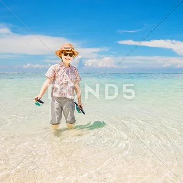 Happy kid boy wearing summer hat and hipster sunglasses walks in shallow water Stock Photos