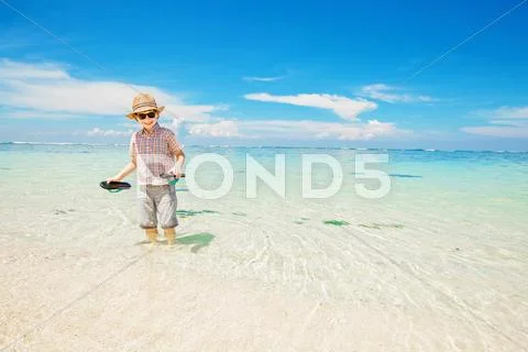 Happy kid boy wearing summer hat and hipster sunglasses walks in shallow water Stock Photos