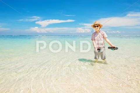 Happy kid boy wearing summer hat and hipster sunglasses walks in shallow water Stock Photos