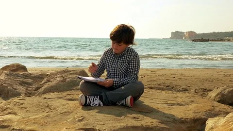 Happy kid doing homework in front of the ocean at sunset dolly shot Stock Footage 79625191