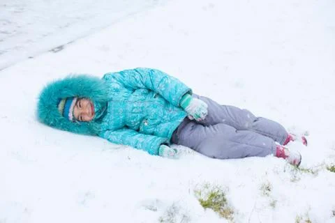 Happy kid girl child outdoors in winter lying on snow Stock Photos