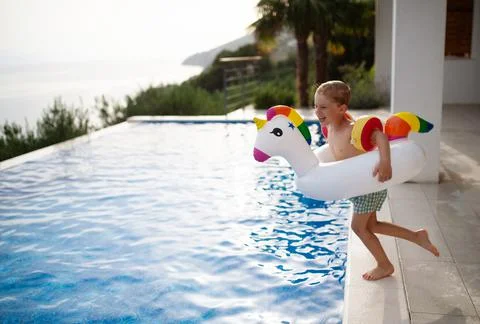 Happy kid having fun when jumping to swimming pool with inflatable ring unicorn Stock Photos