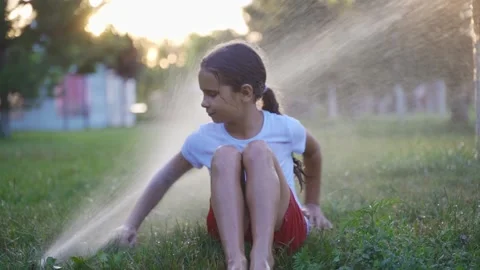 Happy kid play with a stream of water from a lawn sprinkler. playing outdoors in Stock Footage