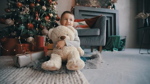 Happy kid with teddy bear sitting near the xmas tree Stock Footage 122016412