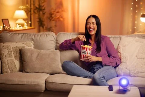 Happy lady laughing while watching funny movie, holding bucket of popcorn in Foto stock