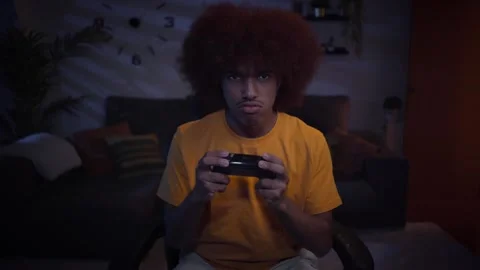 Happy Latin afro man playing video games sitting gamer chair alone in living Stock Footage 249905476