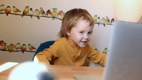 Happy laughing little boy using laptop for video call, looking cartoons and Видео 128925979